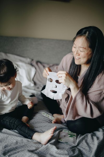 woman sitting on bed making a mask beside her child